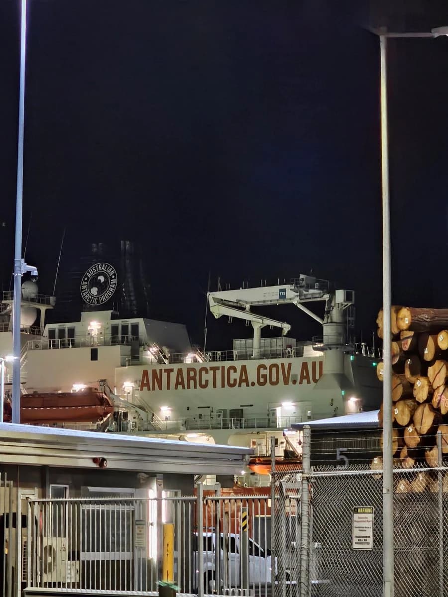 A ship docked at night, with ANTARCTICA.GOV.AU painted on its side and the Australian Antarctic Program emblem on its funnel.