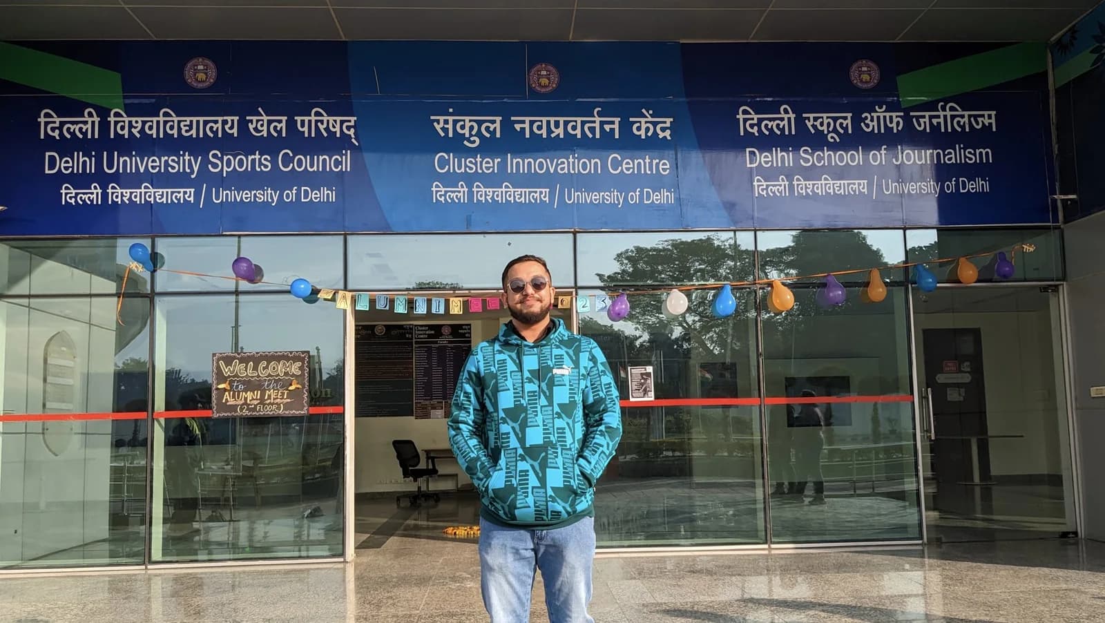 Ashish outside the Cluster Innovation Centre, beneath the signs and decorations for the 2023 alumni meet.