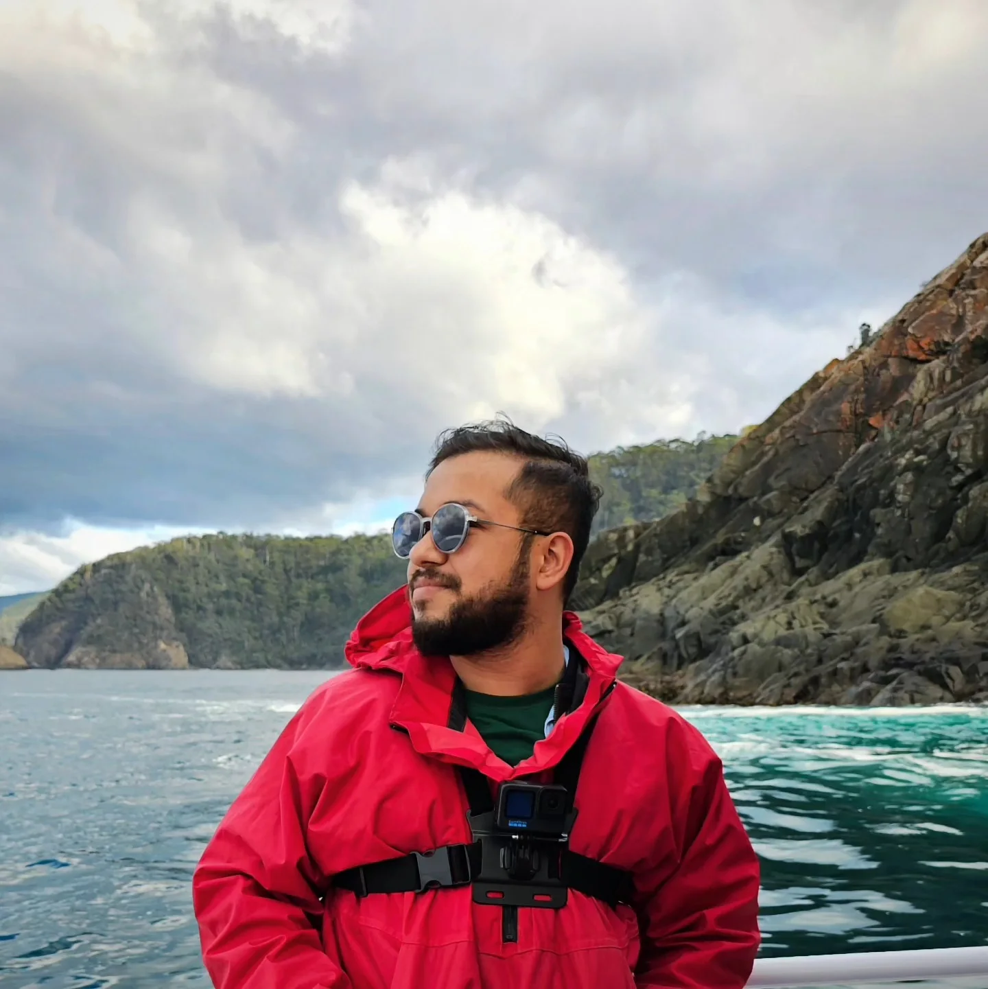 Ashish in a red jacket on a boat, looking toward the cliffs near Bruny Island.