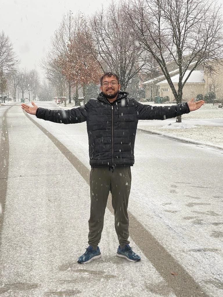 Ashish standing with his arms outstretched on a snow-covered residential street as snow falls.