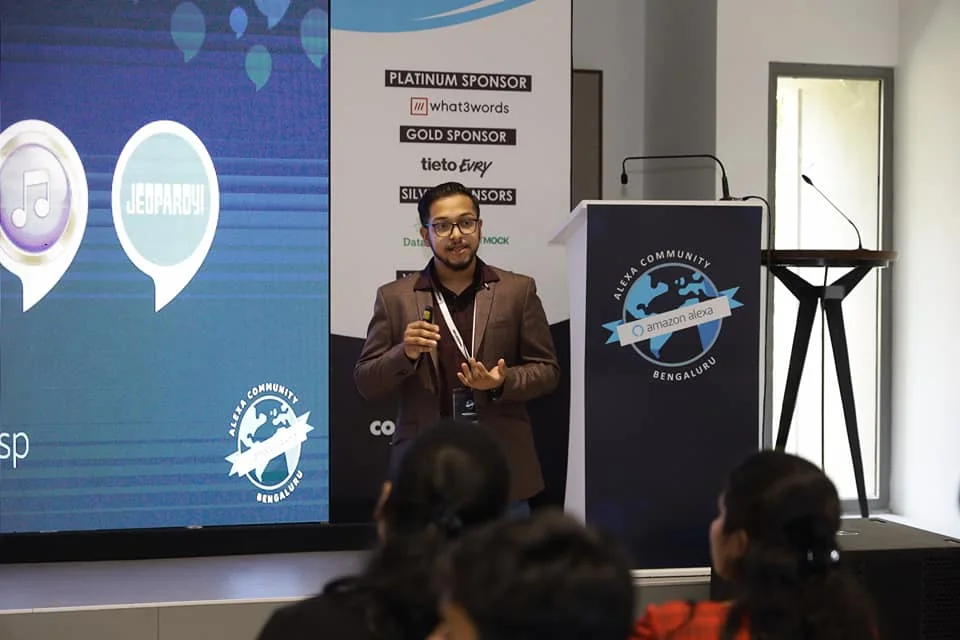 Ashish speaking into a handheld microphone on the Alexa Community Day stage, with the audience in the foreground.