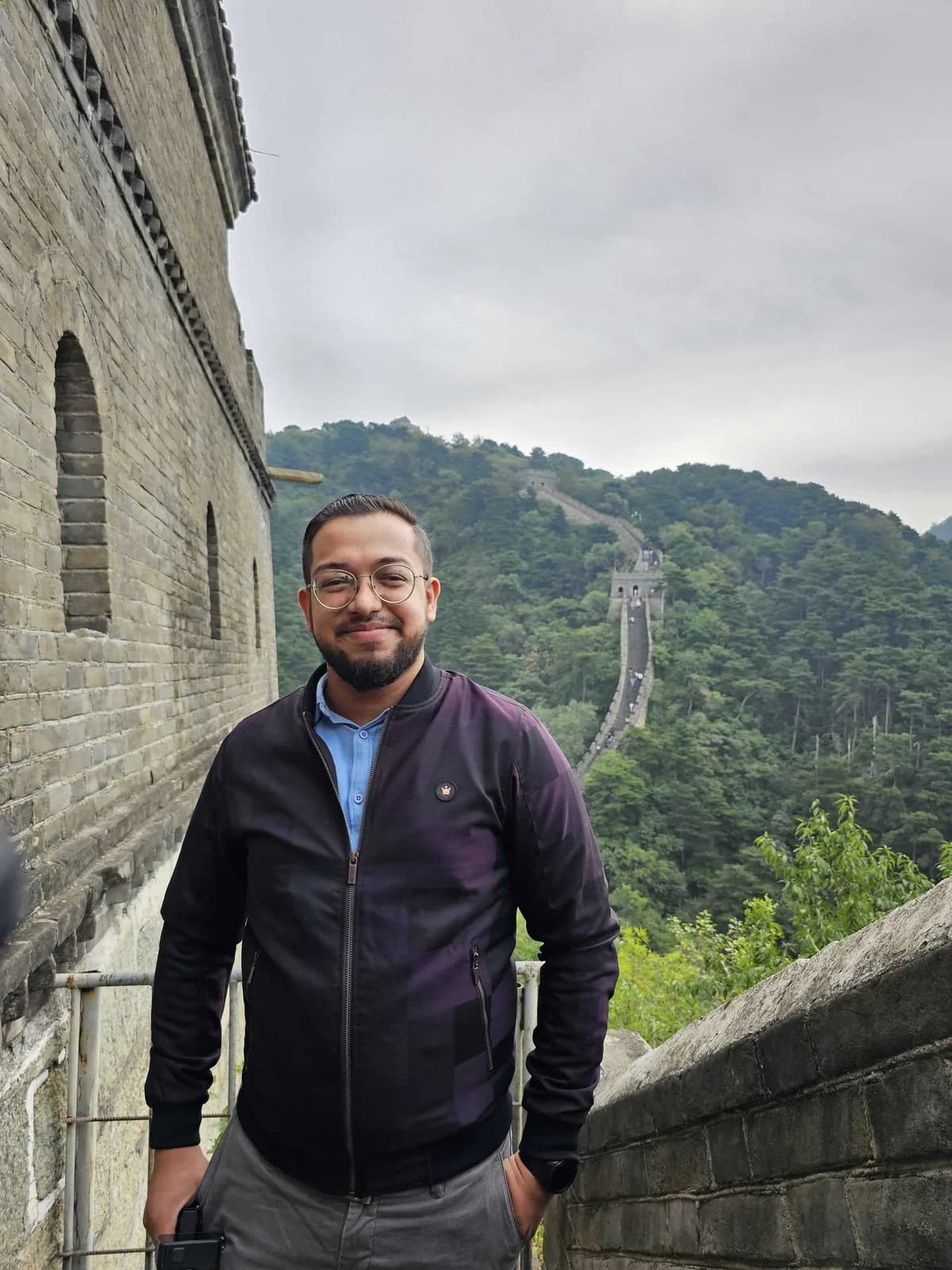 Ashish standing on the Great Wall of China, with wooded hills behind him.
