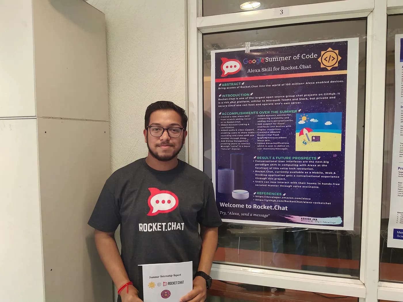 Ashish wearing a Rocket.Chat T-shirt and holding his project report beside the poster for his Google Summer of Code Alexa skill.