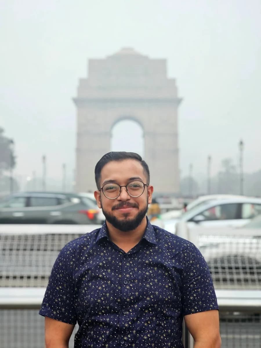 Ashish in a blue patterned shirt, with India Gate in the hazy Delhi background.