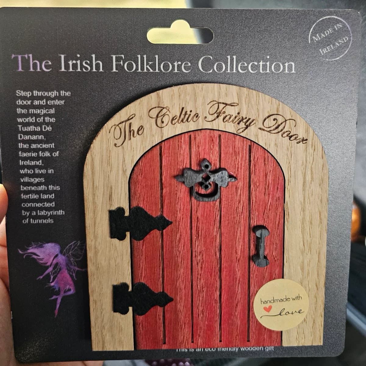 A tiny red wooden Celtic fairy door, still on its Irish Folklore Collection backing card.