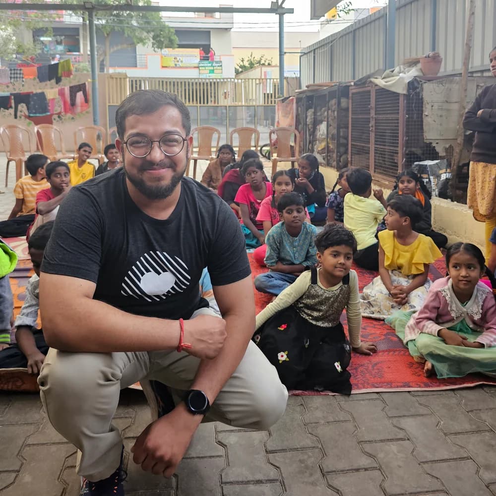 Ashish crouching and smiling, with a group seated behind him at Jeevitha orphanage.