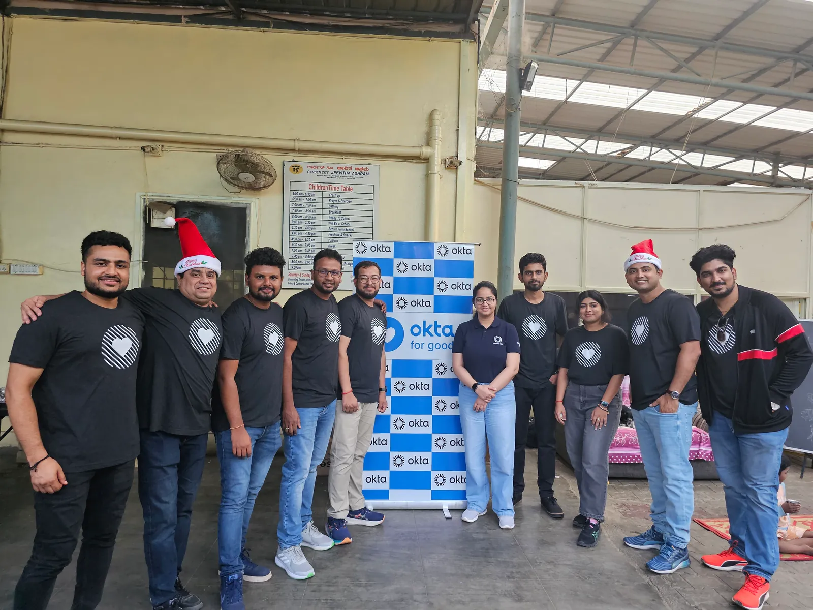 The volunteer team standing together beside the Okta for Good banner at Jeevitha.