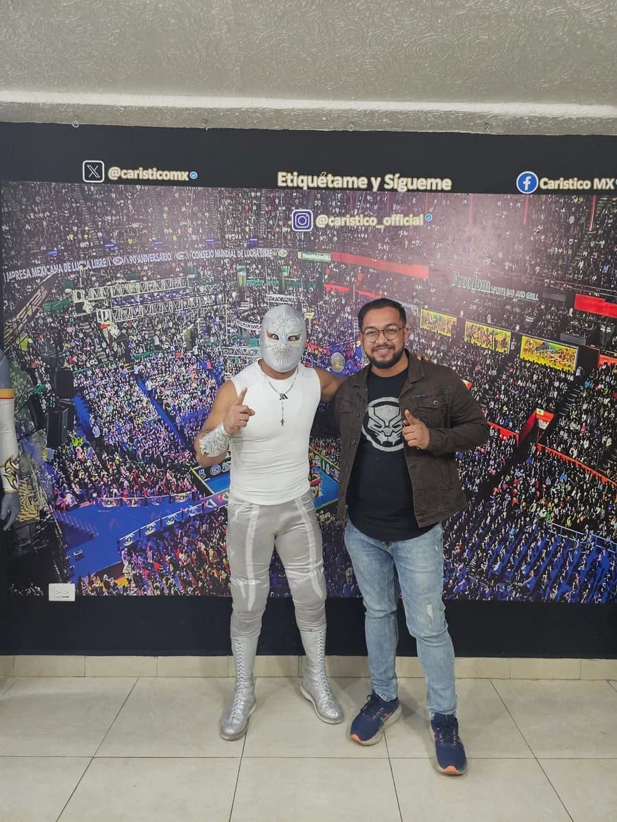 Ashish and a luchador in a silver mask standing together, both giving a thumbs-up, in front of a wrestling-arena backdrop.