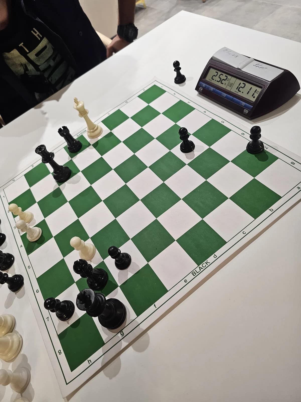 Pieces on a green-and-white chessboard beside a digital chess clock at an office tournament.