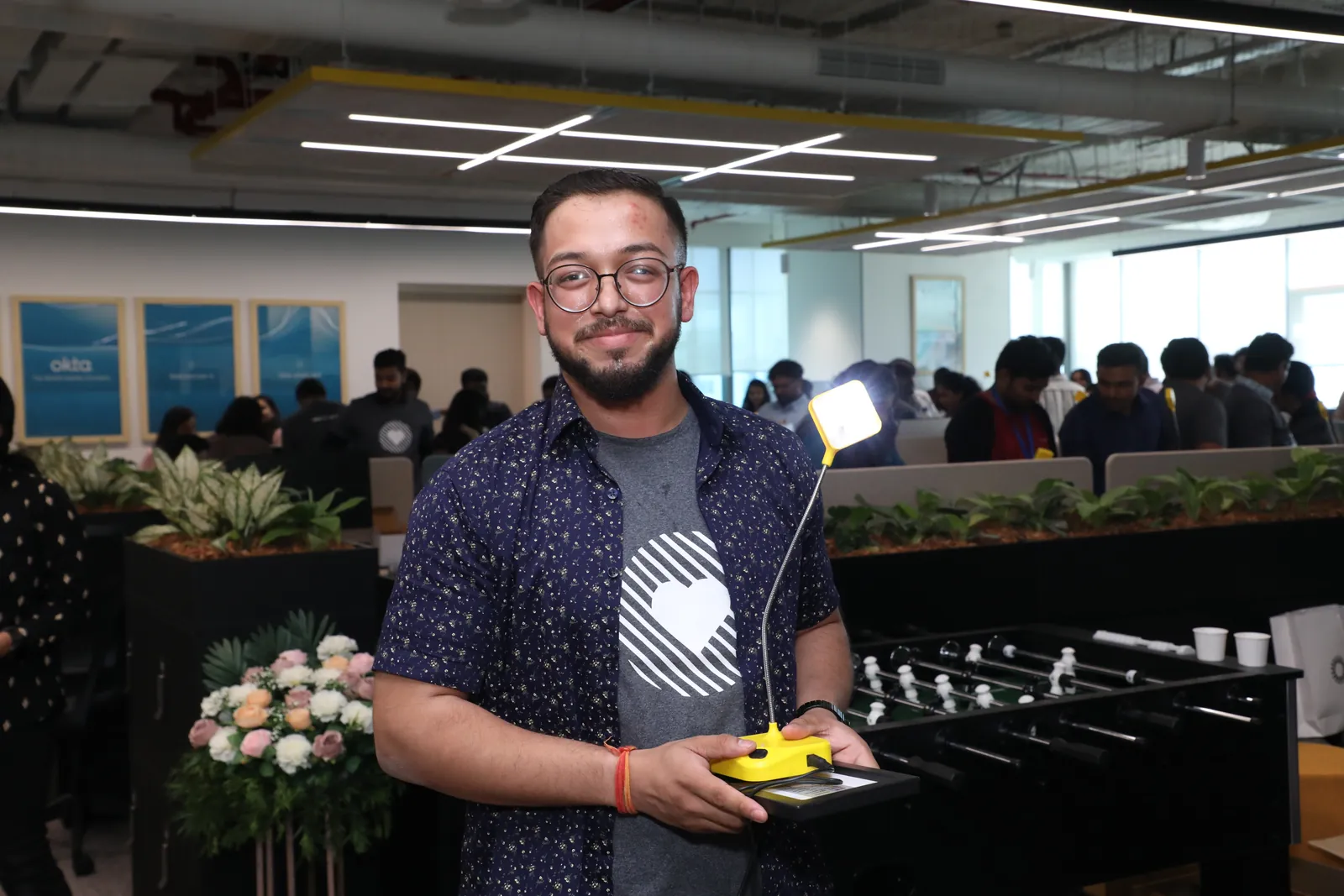 Ashish holding an assembled yellow solar lamp and its solar panel in the office.