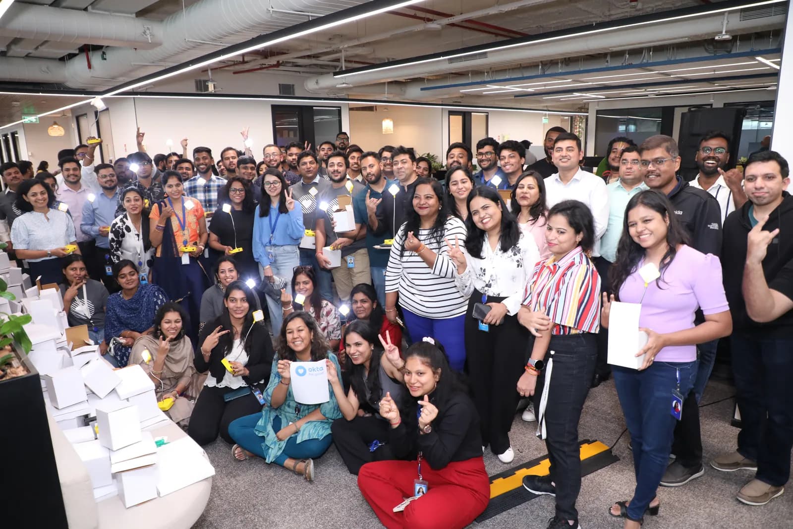 A large group of Okta colleagues holding their assembled yellow study lamps.