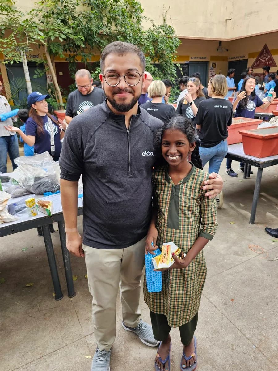 Ashish standing beside a smiling pupil in the school courtyard, with other volunteers behind them.