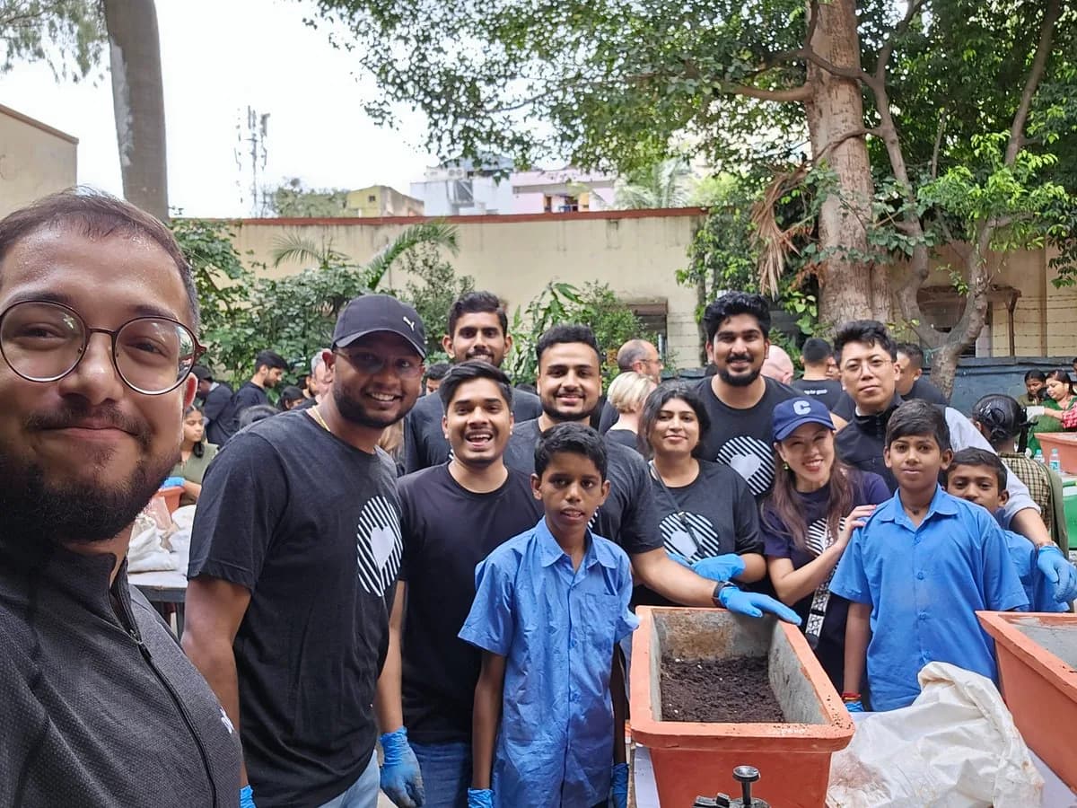 A group selfie of Ashish, Okta colleagues and pupils gathered around planters in a school courtyard.