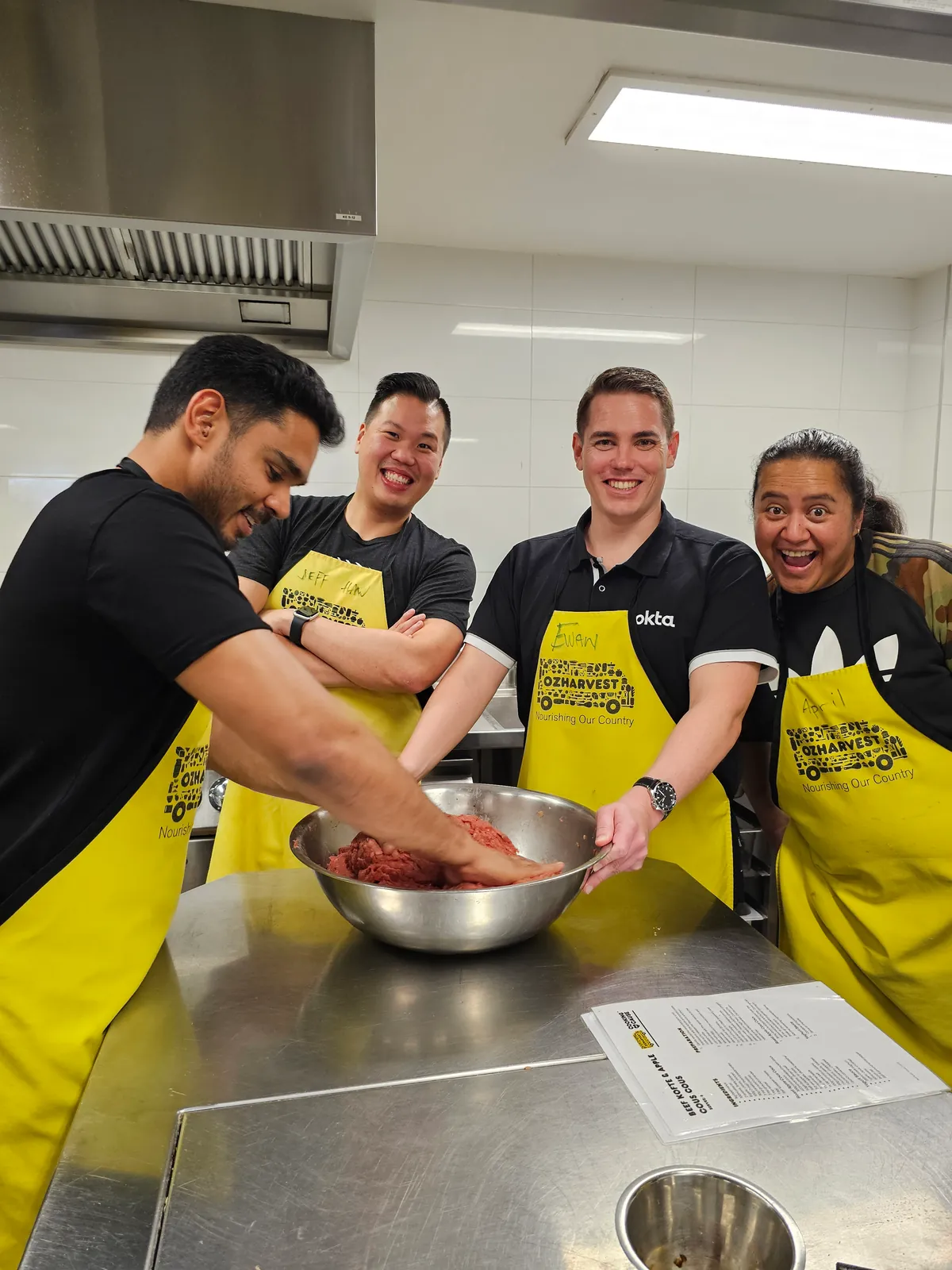 Colleagues in yellow OzHarvest aprons preparing ingredients together at a kitchen bench.