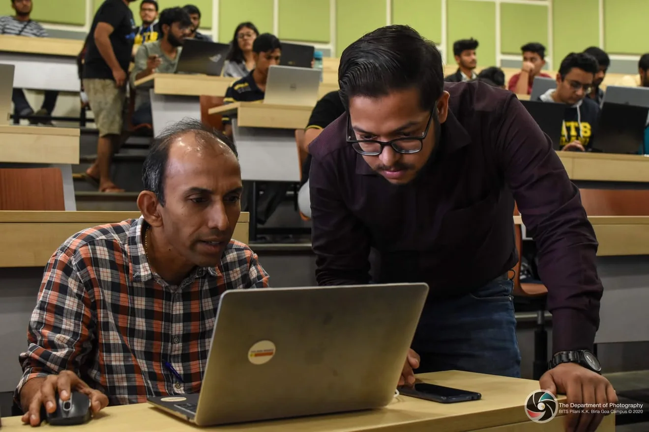 Ashish leaning over a laptop to help a participant during the Quark workshop, with other learners working behind them.