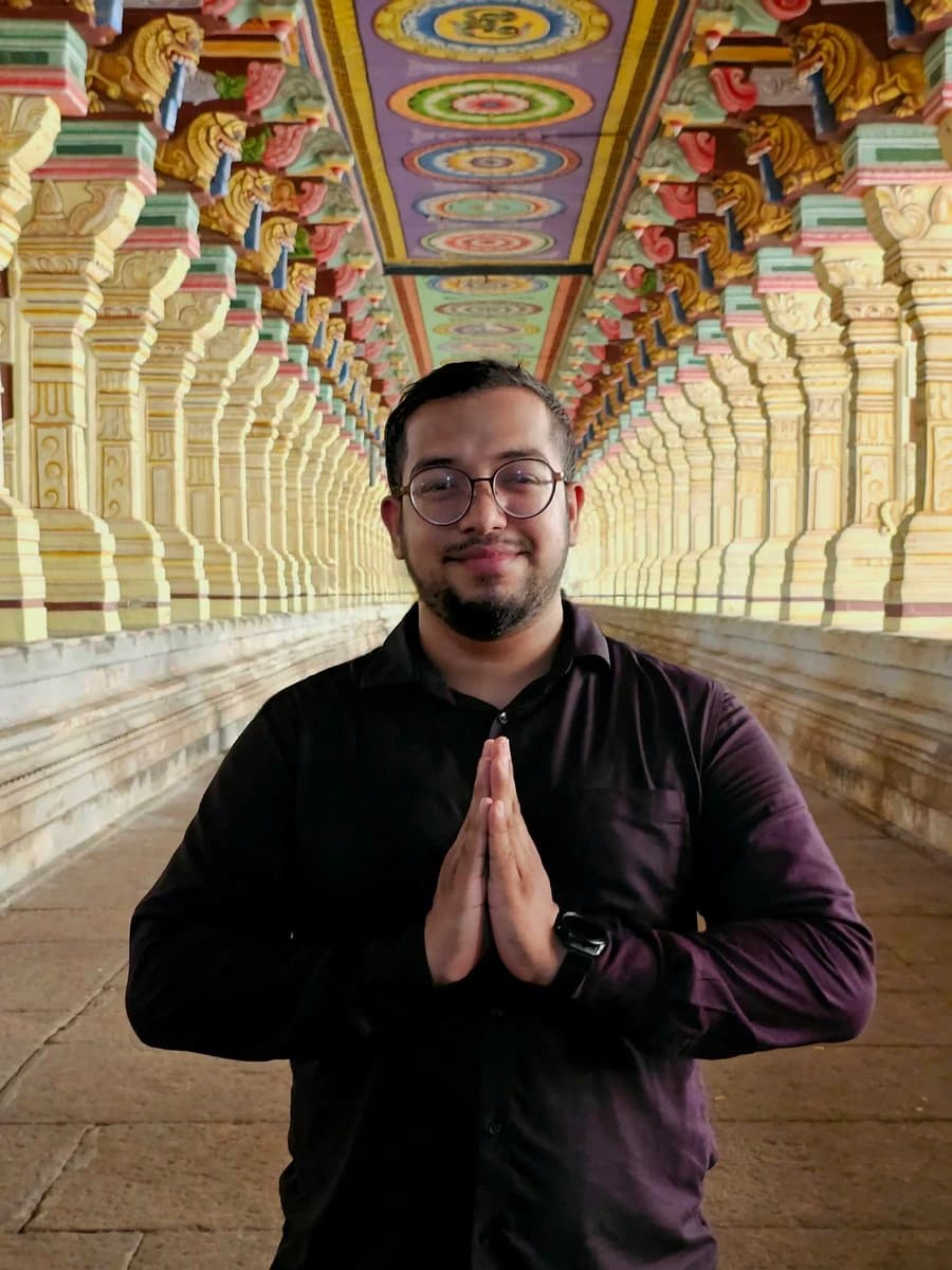 Ashish with his palms together in a corridor of painted pillars at Ramanathaswamy Temple.