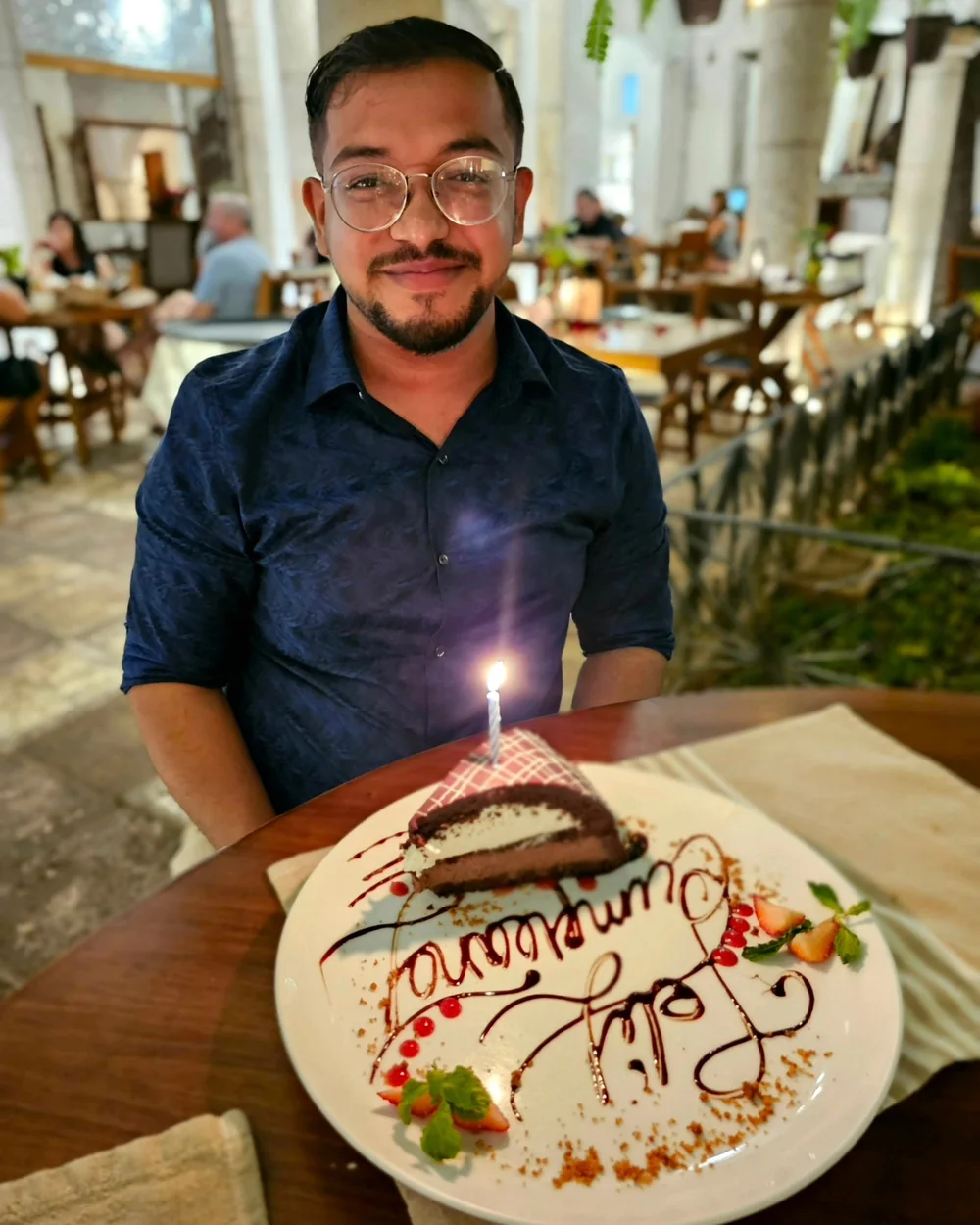Ashish smiling behind a birthday cake with a lit candle in Valladolid, Mexico.