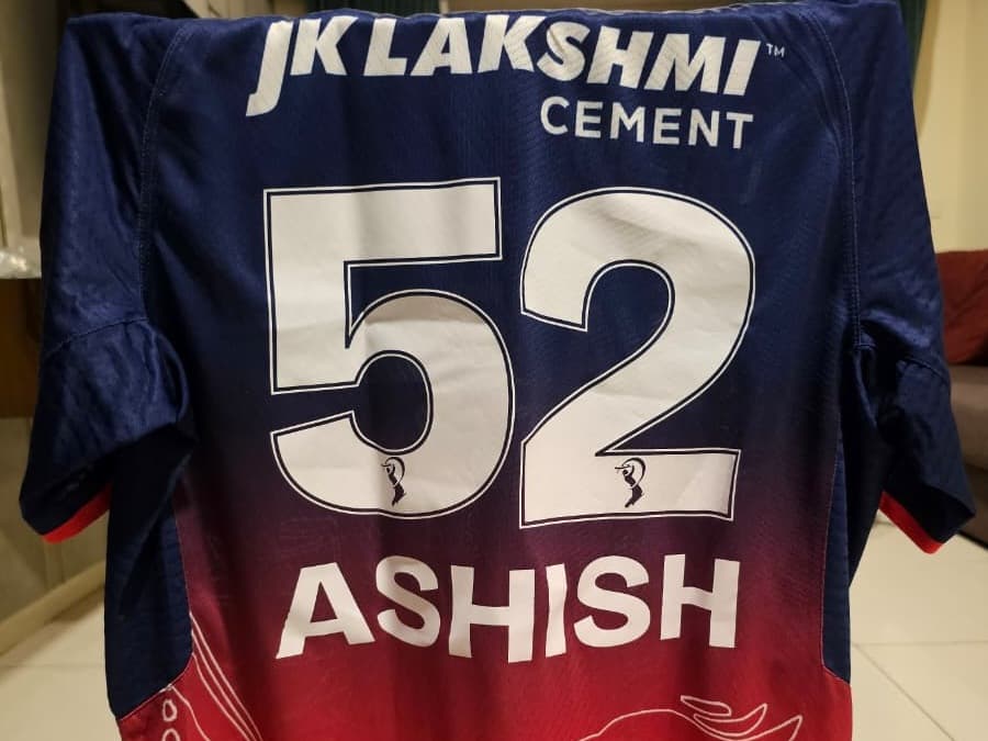 The back of a Rajasthan Royals 2026 shirt: JK Lakshmi Cement across the shoulders, the number 52 in large white figures, and ASHISH printed below it.